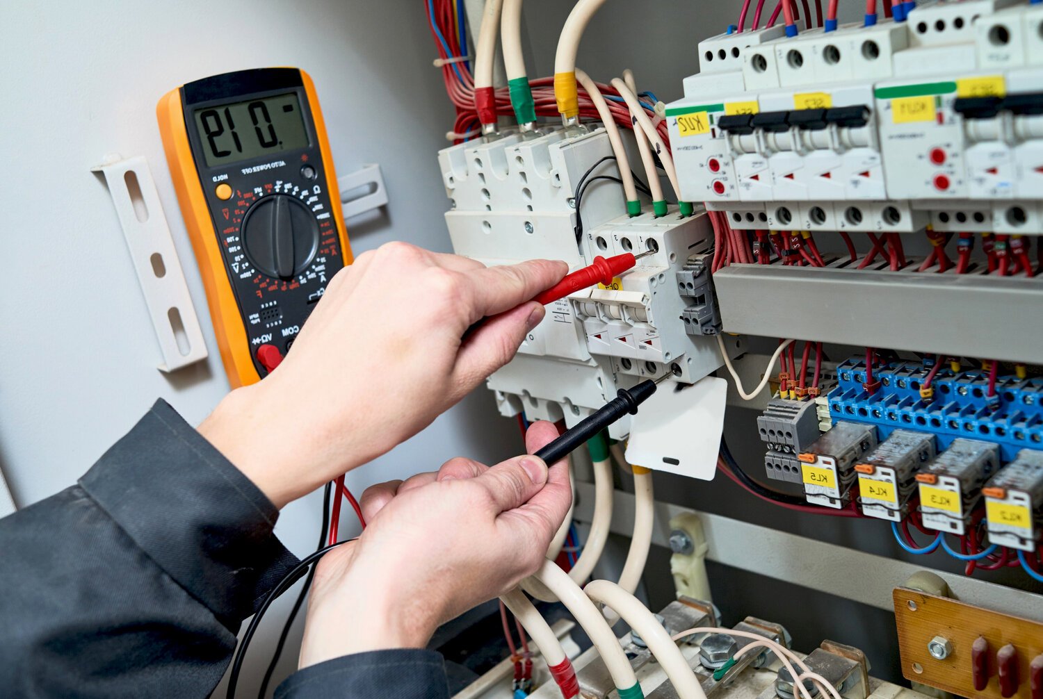Электрик измеряет напряжение в электрощите мультиметром. Проверка электропроводки и автоматических выключателей.